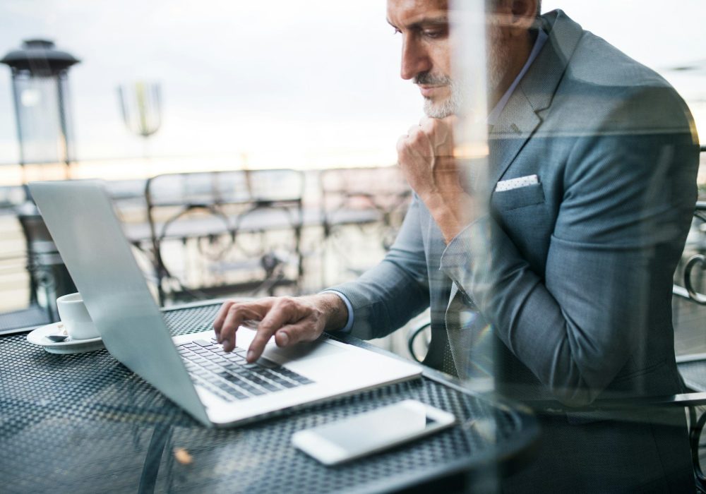 Mature businessman with laptop outside a cafe.